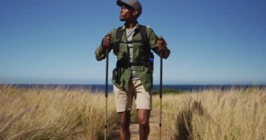 Afrika kökenli Amerikalı bir adam, sahil kenarındaki kırsal kesimde yürüyüş direkleri ile yürüyüş yapıyor. Fitness eğitimi ve sağlıklı açık hava yaşam tarzı..