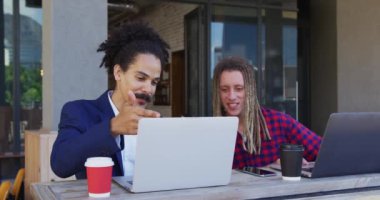 İki farklı erkek arkadaş kafenin dışında oturmuş kahve içiyor ve dizüstü bilgisayar kullanıyor. Dijital göçebeler, şehirde geziyorlar..