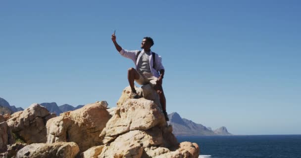 Afrykański Amerykanin Wędrujący Górach Robiący Selfie Siedząc Skale Przy Wybrzeżu — Wideo stockowe