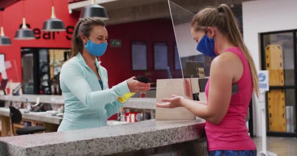 两名戴面具的高加索女人在体育馆的接待处与消毒手交谈 食管癌大流行期间的健康与休闲D — 图库视频影像
