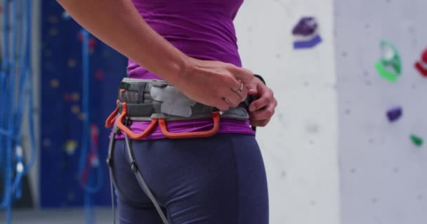 屋内クライミングウォールで登るためのクライミングハーネスベルトを準備白人女性 フィットネス レジャータイム — ストック動画