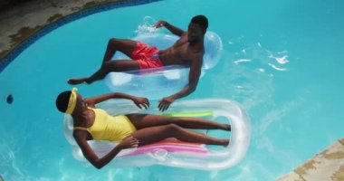 Mutlu Afro-Amerikan çifti yüzme havuzunda şişme masalara uzanmış birbirlerine su sıçratıyor ve gülümsüyor. Karantina süresince evde tecrit altında kalmak.