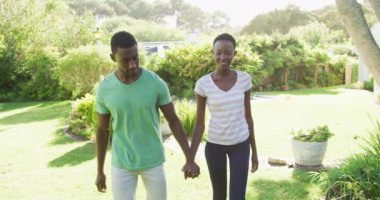 Gülümseyen Afrikalı Amerikalı çift güneşli bahçede el ele yürüyor. Karantina süresince evde tecrit altında kalmak.