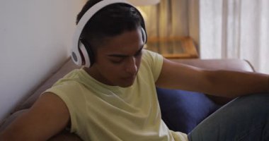 Kulaklık takan melez yarışçı koltukta oturmuş akıllı telefon kullanıyor ve gülüyor. Karantina süresince evde tecrit altında kalmak.