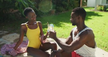 Mutlu Afro-Amerikan çifti güneşli bahçede oturmuş içkileriyle kadeh kaldırıyor. Karantina süresince evde tecrit altında kalmak.