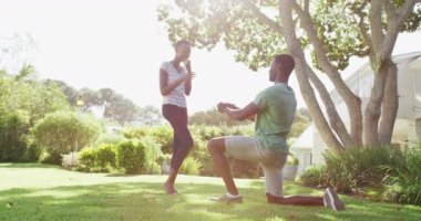 Mutlu Afro-Amerikan çifti Sunny Garden 'da dizlerinin üzerinde yüzüklerini tutarak kadınlara evlenme teklif ediyorlar. Karantina süresince evde tecrit altında kalmak.