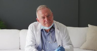 Kafkas kıdemli erkek doktor, yüz maskesi takılı, video görüşmesi yaparken not alıyor. uzaktan iletişim ve teletıp danışma kavramı.