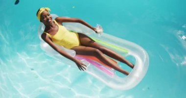 Çekici Afrikalı Amerikalı kadın şişme bir içkinin üzerinde uzanıyor ve yüzme havuzunda gülümsüyor. Karantina süresince evde tecrit altında kalmak.