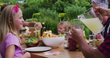 Bahçedeki aile yemeğinde limonata içen gülümseyen beyaz kız. Üç kuşak aile, dışarıda birlikte yemek yemeyi kutluyor..