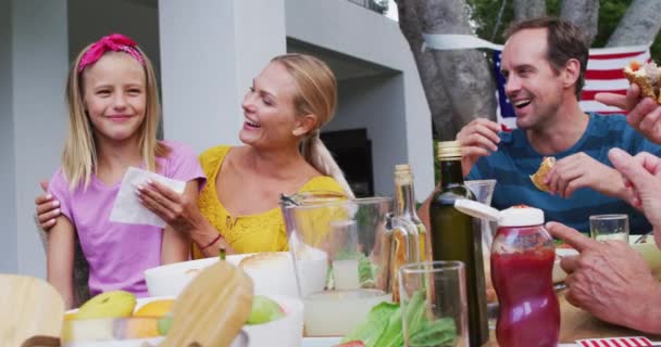 庭で家族のお祝いの食事中に娘の顔を拭く笑顔白人女性 独立記念日を祝う3世代家族で一緒に屋外で食べる Aufa — ストック動画