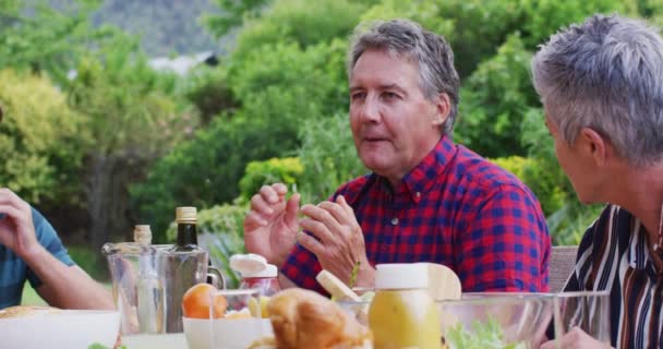 庭で家族のお祝いの食事中に話している白人の高齢者 屋外で一緒に食べることを祝う3世代家族 — ストック動画