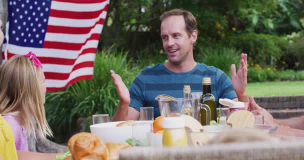 庭で家族のお祝いの食事中に話す笑顔の白人男性 独立記念日を祝う家族みんなで屋外で食事 — ストック動画