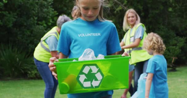 リサイクルボックスを持った笑顔の白人女の子がボランティアと一緒にゴミを拾います 生態系保全ボランティアが田舎で掃除をしています — ストック動画
