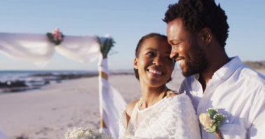 Afrika kökenli Amerikalı çift evleniyor ve kumsalda gülümsüyor. Evlilik, aşk ve romantizm, deniz kenarında tatil.