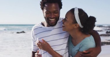 Gülümseyen, kucaklayan ve sahilde yürüyen Afrikalı Amerikalı çift. sağlıklı açık hava eğlence zamanı deniz kenarında.
