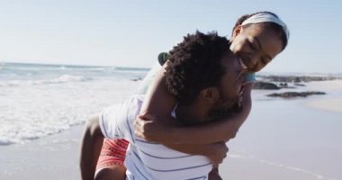 Afrika kökenli Amerikalı bir adam, Afrika kökenli Amerikalı bir kadını kumsalda sırtında taşıyor. sağlıklı açık hava eğlence zamanı deniz kenarında.