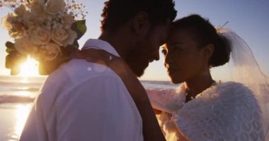 Aşık Afrikalı Amerikalı çift evleniyor, gün batımında sahilde birbirlerine bakıyorlar. Evlilik, aşk ve romantizm, deniz kenarında tatil.