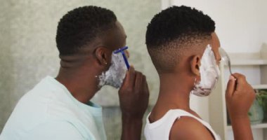 Afrikalı Amerikalı baba ve oğlu birlikte tıraş oluyor. Karantina süresince evde tek başına kalmak..