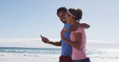 Afrika kökenli Amerikalı çift sahilde akıllı telefonlarıyla selfie çekerken gülümsüyor. sağlıklı açık hava eğlence zamanı deniz kenarında.