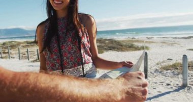 Kumsalda durup harita okuyan beyaz bir çift. Yaz tatili gezisinde plaj durağı.