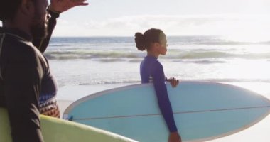 Sahilde sörf tahtası taşıyan Afrikalı Amerikalı bir çift. Tatil ve deniz kenarında sağlıklı vakit geçirme zamanı..