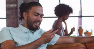 Kafede oturup akıllı telefondan konuşan ve gülümseyen mutlu bir melez. dijital göçebe hareket halinde.