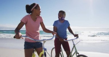 Sahilde gülümseyen ve bisiklete binen Afrikalı Amerikalı çift. sağlıklı açık hava eğlence zamanı deniz kenarında.