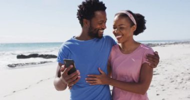 Afrika kökenli Amerikalı çift sahilde akıllı telefonlarıyla selfie çekerken gülümsüyor. sağlıklı açık hava eğlence zamanı deniz kenarında.