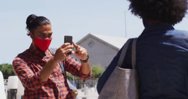 Çeşitli meslektaşlar yüz maskesi takıp akıllı telefon kullanarak fotoğraf çekiyorlar. Dijital göçebeler Coronavirus covid 19 salgını sırasında hareket halindeler..