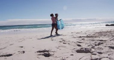 Afrika kökenli Amerikalı bir çift çöp torbalarıyla yürüyor ve sahilden çöp topluyorlar. Eko Sahili Koruma.