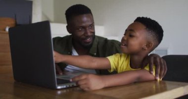 Afrikalı Amerikalı baba ve oğlu birlikte dizüstü bilgisayar kullanıyorlar. Karantina süresince evde tek başına kalmak..