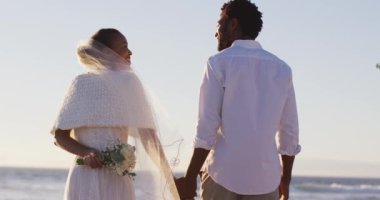 Aşık Afrikalı Amerikalı çift evleniyor, birbirlerine bakıyor, sahilde el ele tutuşuyorlar. Evlilik, aşk ve romantizm, deniz kenarında tatil.