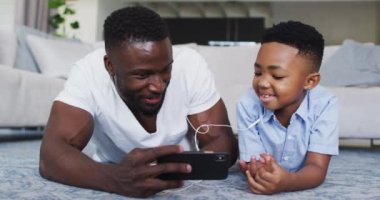 Afrika kökenli Amerikalı baba ve oğul kulaklık takıyor ve akıllı telefon kullanıyor. Karantina süresince evde tek başına kalmak..