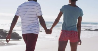 Gülümseyen, el ele tutuşan ve sahilde yürüyen Afrikalı Amerikalı çift. sağlıklı açık hava eğlence zamanı deniz kenarında.