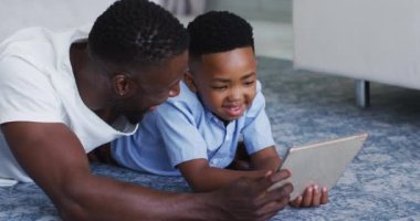 Afrikalı Amerikalı baba ve oğlu dijital tablet kullanıyorlar. Karantina süresince evde tek başına kalmak..