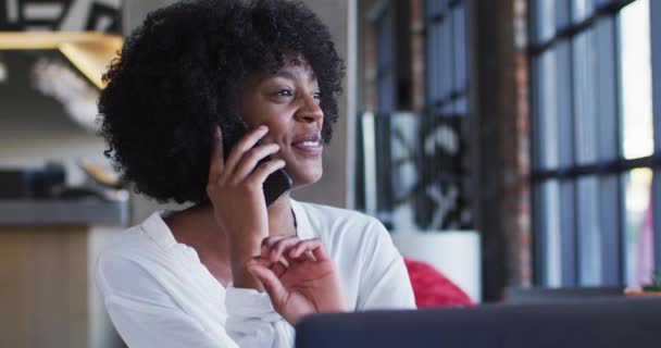 幸せなアフリカ系アメリカ人の女性がカフェでスマートフォンや笑顔で話して座っている 外出先でデジタルノマド — ストック動画