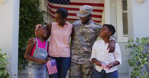 幸せなアフリカ系アメリカ人男性兵士の家やアメリカ国旗の前で妻と子供を受け入れる 兵士は家族の元に戻り — ストック動画