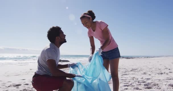 アフリカ系アメリカ人のカップルは ゴミ袋を持っていて ビーチからゴミを収集しています エコビーチの保全 — ストック動画