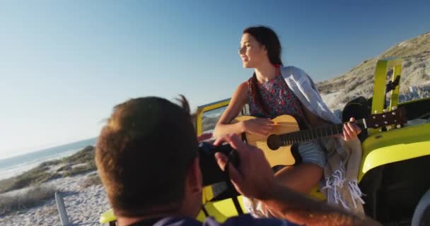 Fehér Férfi Fényképeket Készít Egy Nőről Aki Tengerparti Hintóban Gitározik — Stock videók