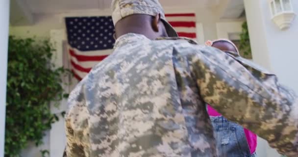 アフリカ系アメリカ人兵士の父親はアメリカ国旗を掲げた笑顔の娘を家の前で抱きかかえていた 兵士は家族の元に戻り — ストック動画