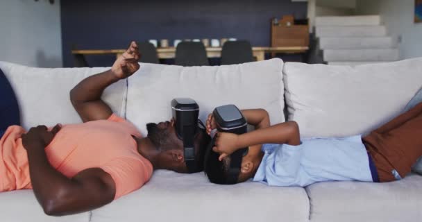 アフリカ系アメリカ人の父親と息子がソファで一緒にVrヘッドセットを使用しています 隔離されたまま家にいると — ストック動画