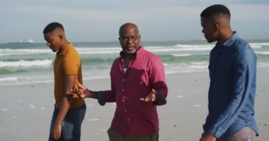 Afrikalı Amerikalı kıdemli baba ve ikiz oğulları sahilde yürüyor ve konuşuyorlar. Sağlıklı açık hava aile birlikte zaman geçirir..