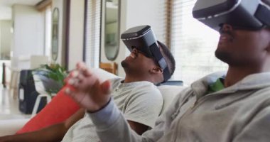 İki Afro-Amerikalı genç ikiz kardeş kanepeye oturmuş VR kulaklıklar takıyor ve gülümsüyor. Karantina süresince ailece evde vakit geçirmek..