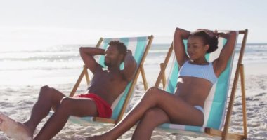 Afrika kökenli Amerikalı çift kumsalda iskemlede otururken güneşleniyor. seyahat romantik tatil yaşam tarzı konsepti