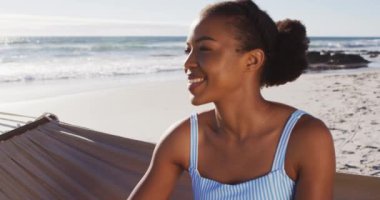 Sahilde bir hamakta otururken gülümseyen Afrikalı Amerikalı kadını yakından çek. seyahat tatil yaşam tarzı konsepti