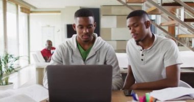 İki Afrikalı Amerikalı genç ikiz kardeş dizüstü bilgisayar kullanıyor ve arka planda babamla konuşuyorlar. Karantina süresince ailece evde vakit geçirmek..