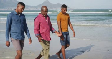 Afrikalı Amerikalı kıdemli baba ve ikiz oğulları sahilde yürüyor ve konuşuyorlar. Sağlıklı açık hava aile birlikte zaman geçirir..