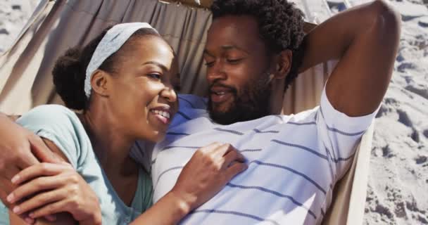 アフリカ系アメリカ人の夫婦が浜のハンモックに寝そべっている ロマンチックな休暇のライフスタイルのコンセプトを — ストック動画