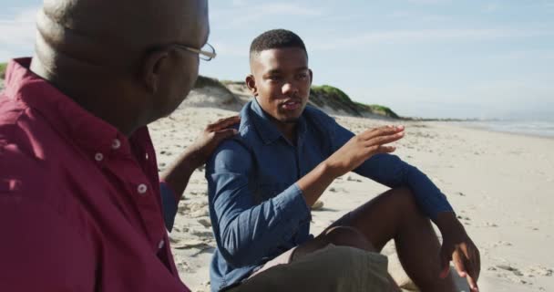 Африканский Отец Американец Сидит Пляже Сыном Подростком Кладет Руку Плечо — стоковое видео