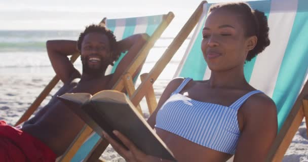 Afrykańska Para Opalająca Się Czytająca Książki Siedząc Leżakach Plaży Podróż — Wideo stockowe